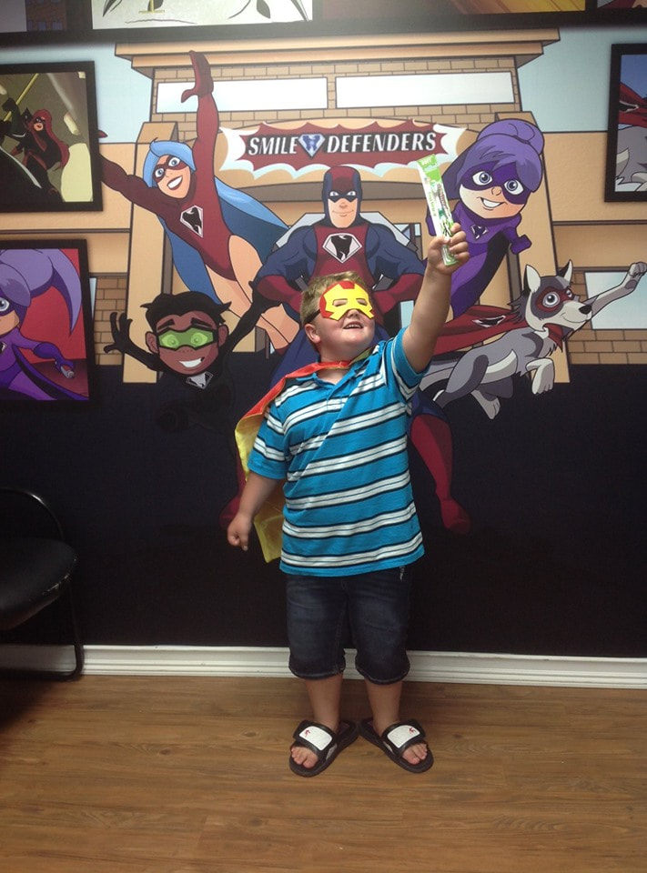 Photo of a young boy wearing a smile defender cape and mask, in a super hero flying pose.