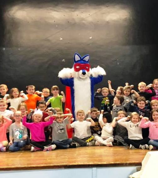 Photo of the Scrubby Mascot, full size adult costume, with a group of school children during a school dental health presentation.